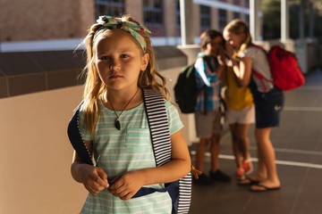 School friends bullying a sad girl in hallway of elementary