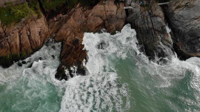 Almost abstract top down aerial view showing the ocean waves rolling in hitting the cliff rocks of Joatinga beach in Rio de Janeiro