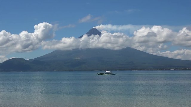 Small boat moves across the ocean in front of Mayon volcano