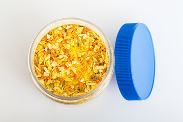 An open jar with universal seasoning on a white background close up. Seasoning contains salt and pieces of dried vegetables and is used for cooking meat, fish, and vegetables. Cooking at home concept