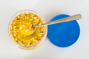 An open jar with universal seasoning on a white background close up. Seasoning contains salt and pieces of dried vegetables and is used for cooking meat, fish, and vegetables. Cooking at home concept