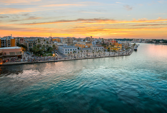 View from a cruise ship as the Piazza Vittorio Emanuele II fills with tourists enjoying a late summer evening sunset at the port city of Brindisi Italy on the Adriatic Coast in the Puglia region.