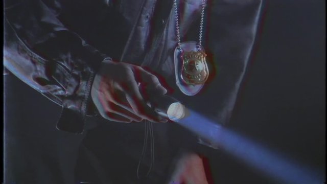 A cop from the past looking around with a flashlight and his police badge. VHS look from the 80s 90s
