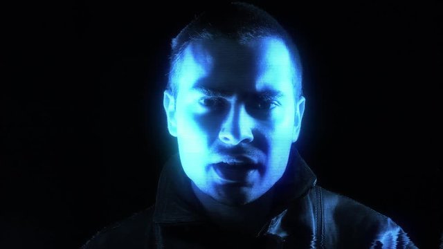 A blue hologram of a man talking seriously to the camera. Black background.