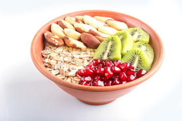 A plate with muesli, kiwi, pomegranate, Brazil nuts isolated on white background.