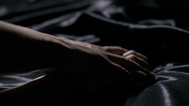 Hot couple holding hands sensually on black silk bed.