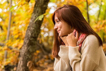 A young red-haired woman warming hands on her scarf in an autumnal forest 