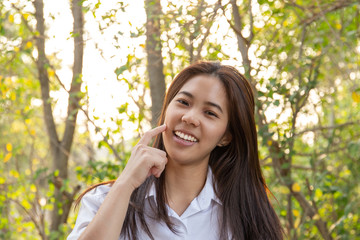 beautiful asian woman with hand on cheek with tree and sunlight in background.