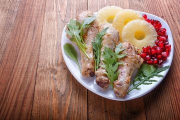 Fried chicken legs with rucola, pineapple and pomegranate seeds on brown wooden background.