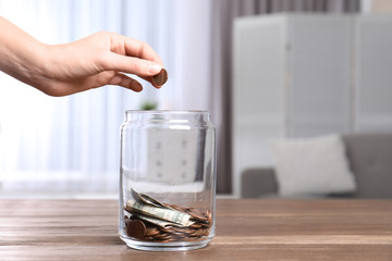Woman putting coin into donation jar on table indoors, closeup. Space for text