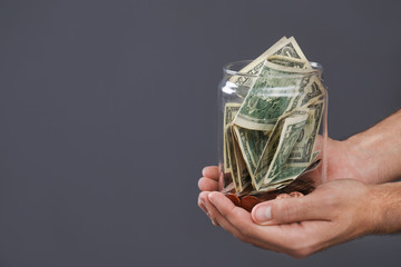Man holding donation jar with money on grey background, closeup. Space for text - obrazy, fototapety, plakaty