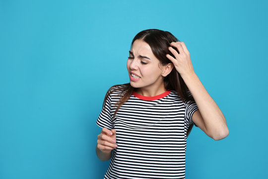 Young woman scratching head on color background. Annoying itch