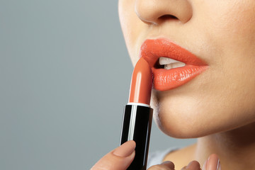 Naklejka premium Young woman applying beautiful lipstick on gray background, closeup. Space for text