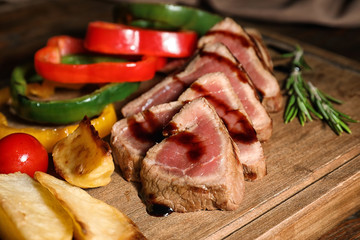 Cut roasted meat served with sauce and garnish on wooden board, closeup