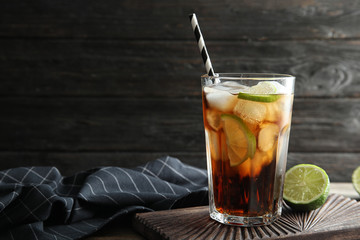 Glass of cocktail with cola, ice and cut lime on table. Space for text