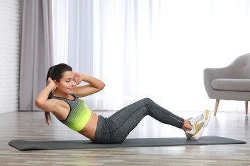 Young woman in fitness clothes doing exercise at home. Space for text