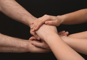 Young people putting their hands together on dark background, closeup