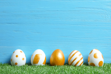 Line of traditional Easter eggs decorated with golden paint on green lawn near wooden wall, space for text