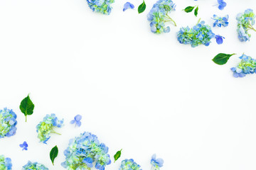 Floral frame of blue hydrangea flowers and leaves on white background. Flat lay, top view.