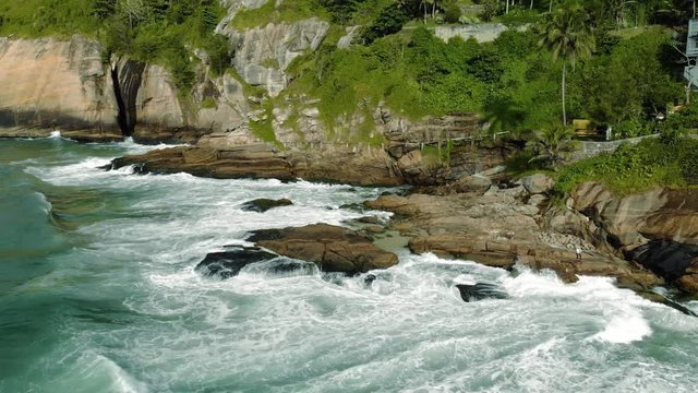 Aerial view of the ocean waves coming in rolling hitting the cliff rocks of Joatinga beach in Rio de Janeiro
