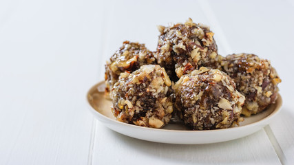 Homemade sweets made of dried fruits and nuts on a plate on a white table.