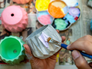 Hand painting pastel purple colour on small concrete planter with blue paintbrush