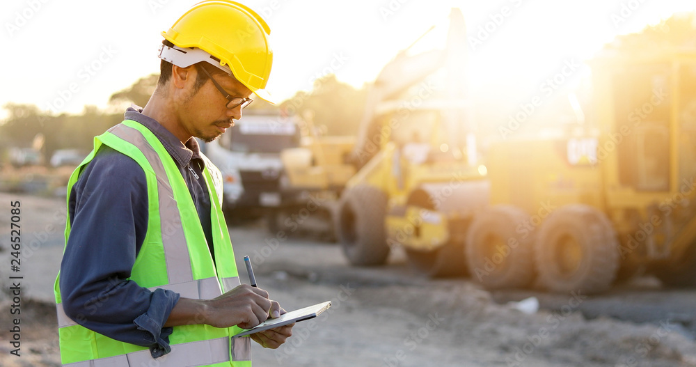 Poster asian engineer with hardhat using tablet pc computer inspecting and working at construction site