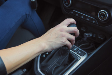 Close up of woman shifting gears on automatic gearbox and driving car. Female hand shifts the hydro...