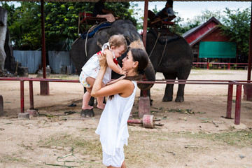 Happy mother and daughter watching and feeding elephants in zoo. Young mother feeds an elephant with her daughter, baby feeds an elephant