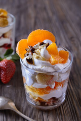 Dessert trifle, cooked at home, with strawberries and orange slices with thick curd cream in a glass beaker on a wooden table