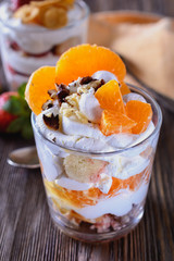 Dessert trifle, cooked at home, with strawberries and orange slices with thick curd cream in a glass beaker on a wooden table