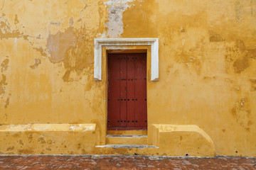 Close up of old wood red door weathered yellow walls on a church in Latin America