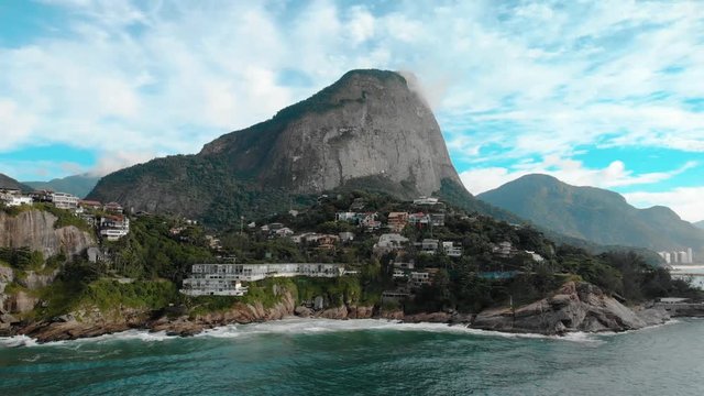Aerial approach of the beautiful picturesque cliff rocks of Joatinga beach in Rio de Janeiro with the Gavea mountain towering behind it and the green ocean waves rolling in
