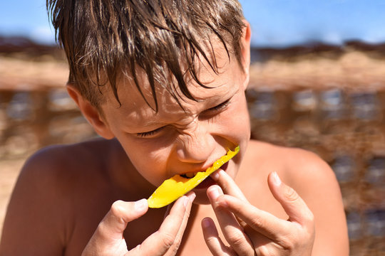 Teenager eating juicy fruit is the mango on the beach, close-up