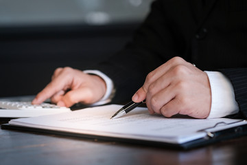 Businessman analyzing investment charts and pressing calculator buttons over documents. Accounting Concept.