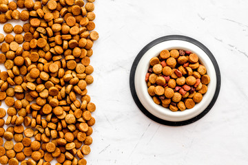 Dry dog food in bowl on white stone backgorund top view space for text pattern