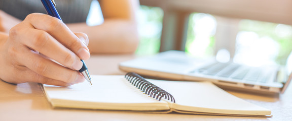Woman hand is writing on notepad with pen in office.