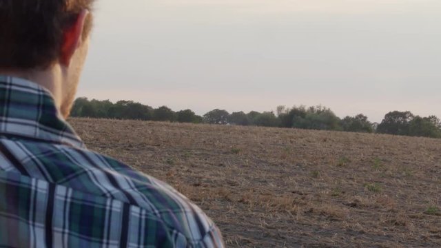 A lost young man with guitar watches the golden sunset on rural field