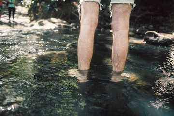 Man crossing the small mountain river bare feet on hiking trail