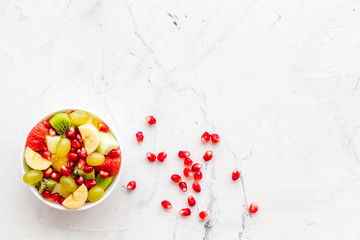 Fruit diet concept. Fruit salad with apple, kiwi and pomegranate in bowl on white stone background top view copy space