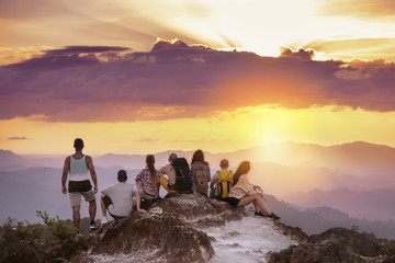 Big group of friends stands on mountain top and looks at beautiful sunset. Travel with friends...