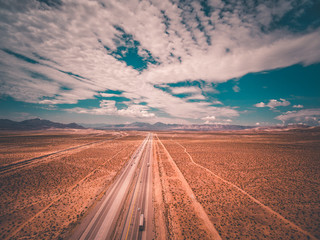 aerial drone shot of a highway leading off into the distance with blue skies and clouds and mountains