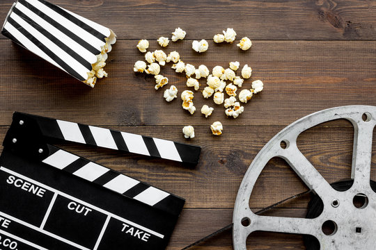 Movie premiere concept. Clapperboard, film stock, popcorn on dark wooden background top view