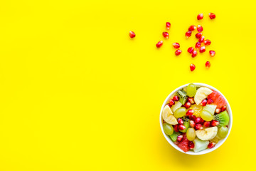 Light healthy breakfast or appetizer. Fruit salad with apple, kiwi and pomegranate in bowl on yellow background top view copy space