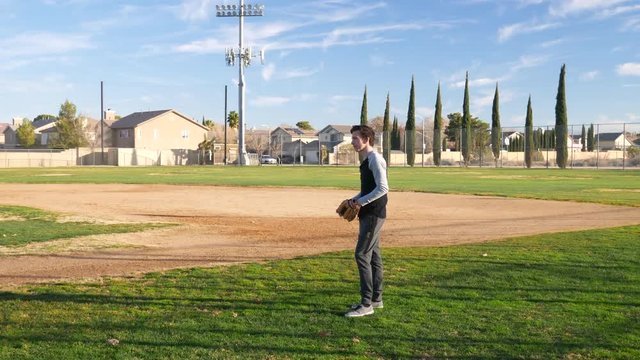 A young man catching and throwing with a baseball and mitt during practice in a grassy park field.