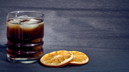 Drink with ice in a stanie on a dark background and oranges.