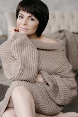 Fototapeta premium Gorgeous young brunette woman in warm knitted sweater posing on the bed in cozy appartments