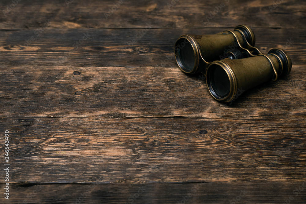 Wall mural Vintage brass binoculars on a brown wooden table background with copy space. Explorer table.