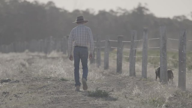 Farmer Walking Along Barbed Wire Fence On Australian Farm