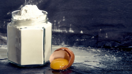 Flour in a jar with a broken egg on a dark background.